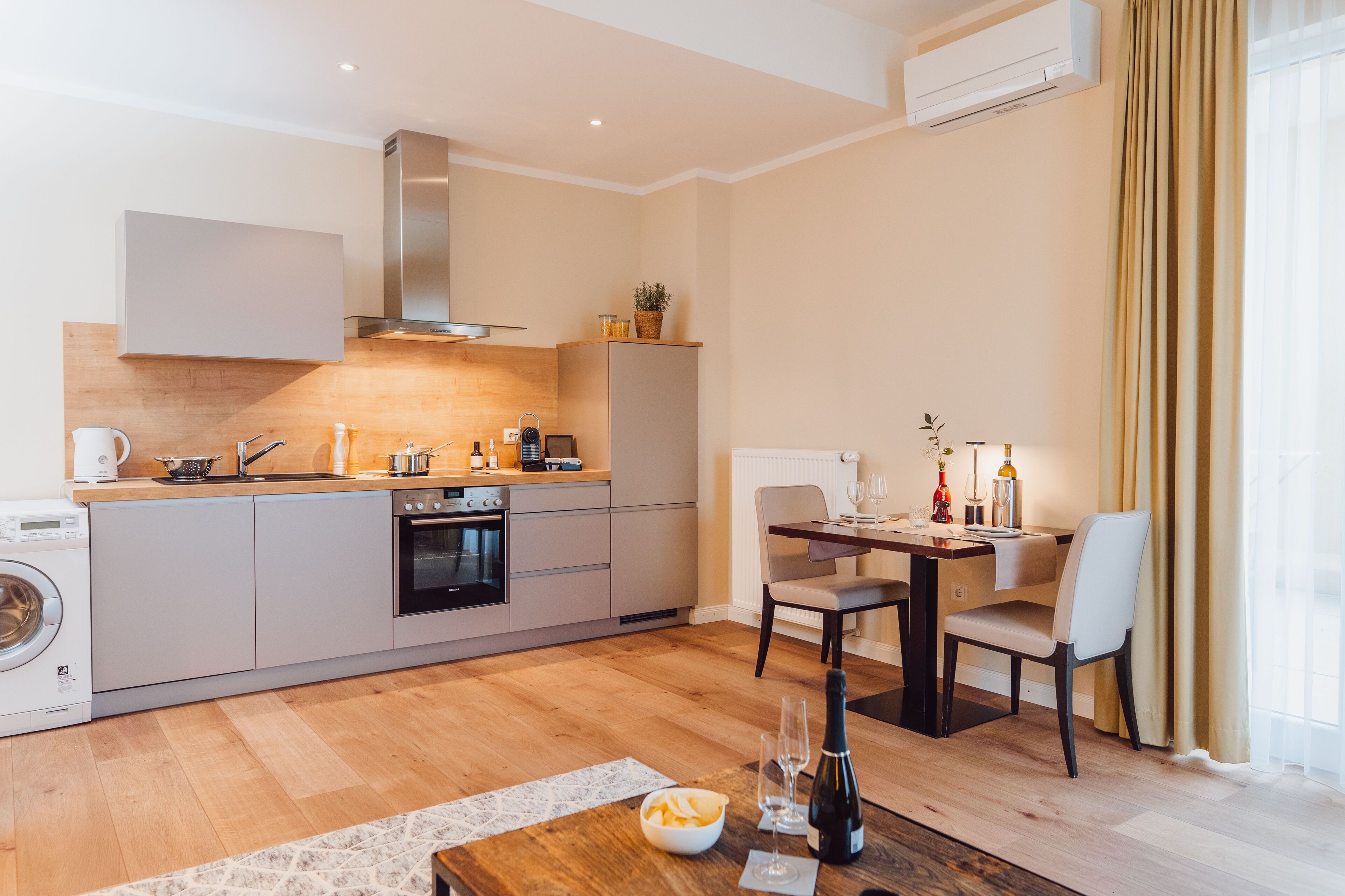 A modern kitchen with a built-in oven, a washing machine, and a dining area with a table and chairs.