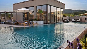 Ein moderner Poolbereich mit klarem, blauen Wasser, Liegestühlen und einer gläsernen Struktur.