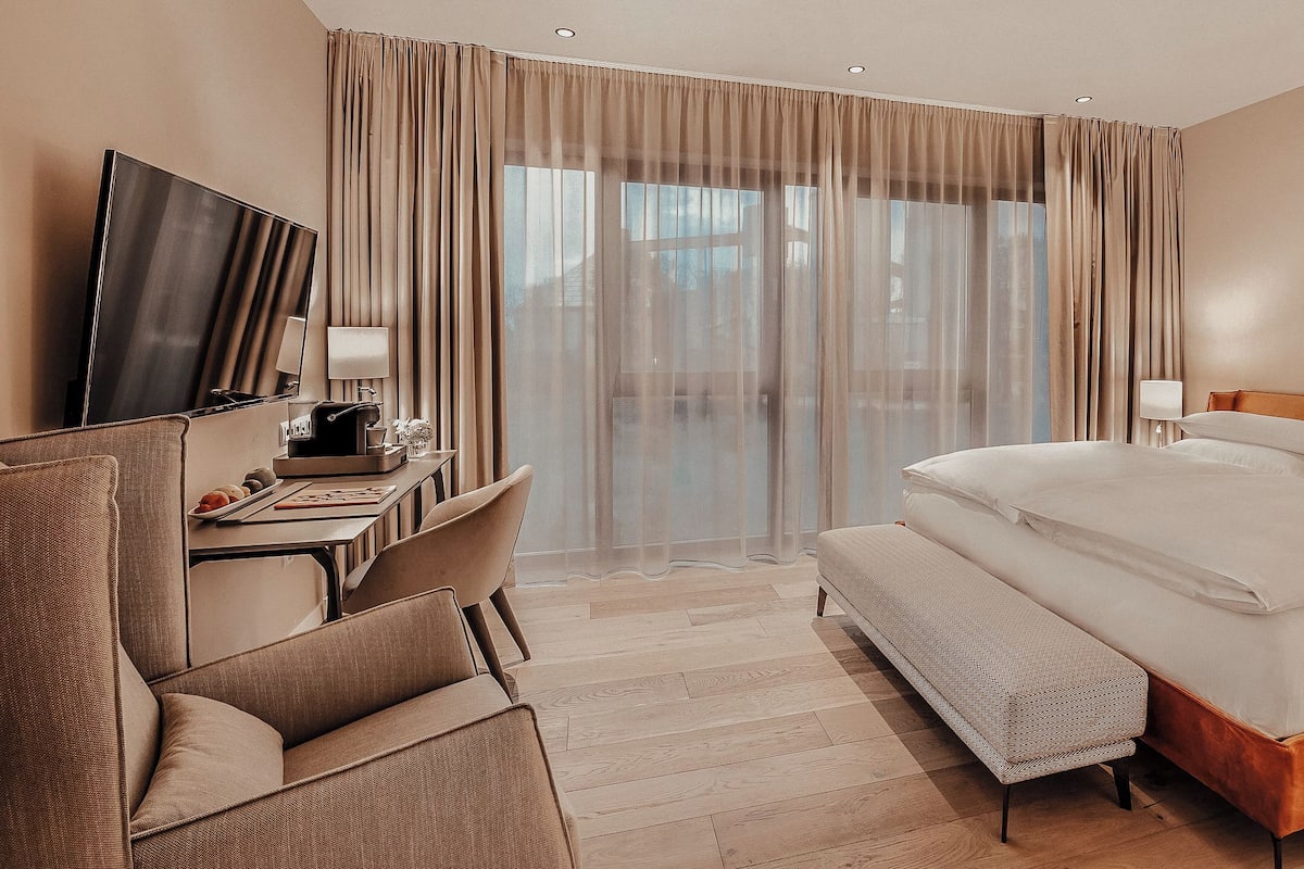 Une chambre d’hôtel avec un grand lit, un bureau avec un ordinateur, une télévision et une vue sur l’extérieur à travers des rideaux transparents.