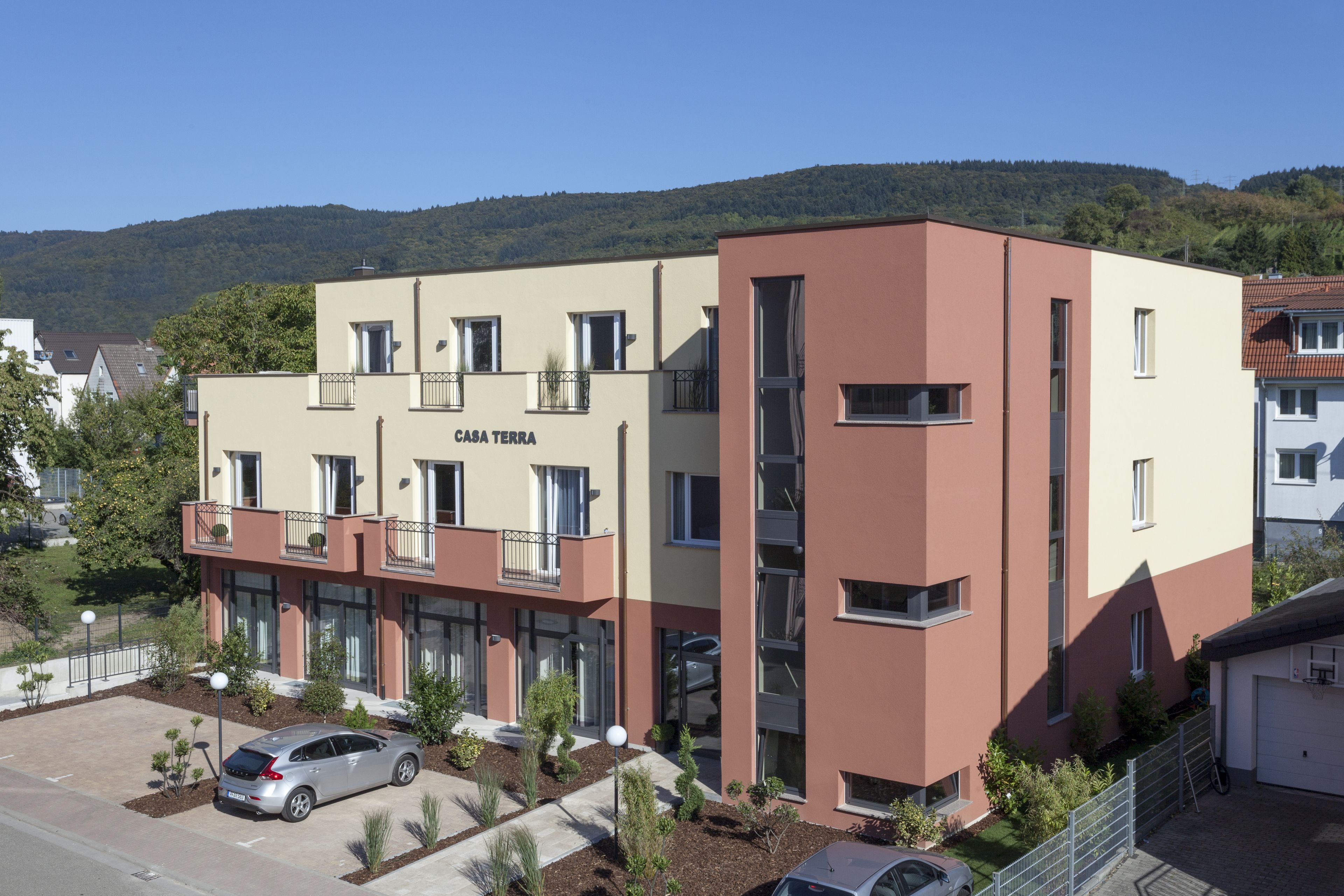 A multi-story building with a sign reading "CASA TERRA." It features a mix of balconies and windows, surrounded by a parking area and small trees.