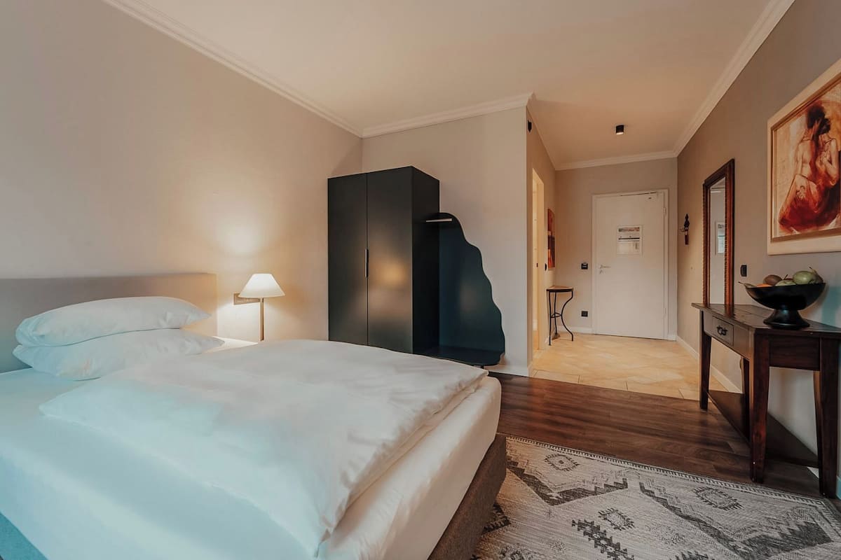 Une chambre d’hôtel avec un lit, un bureau, une chaise, une lampe et un tableau au mur.