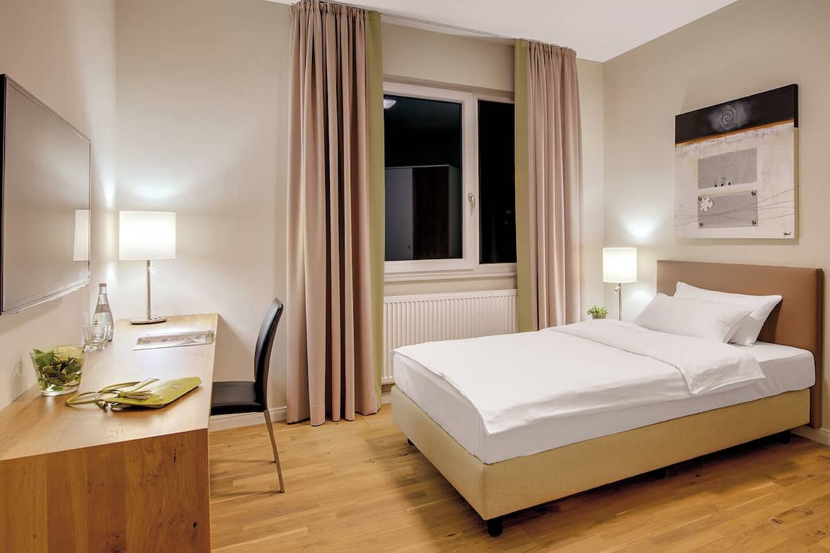 Une chambre d’hôtel avec un lit, une table de chevet, une lampe et une fenêtre avec des rideaux.