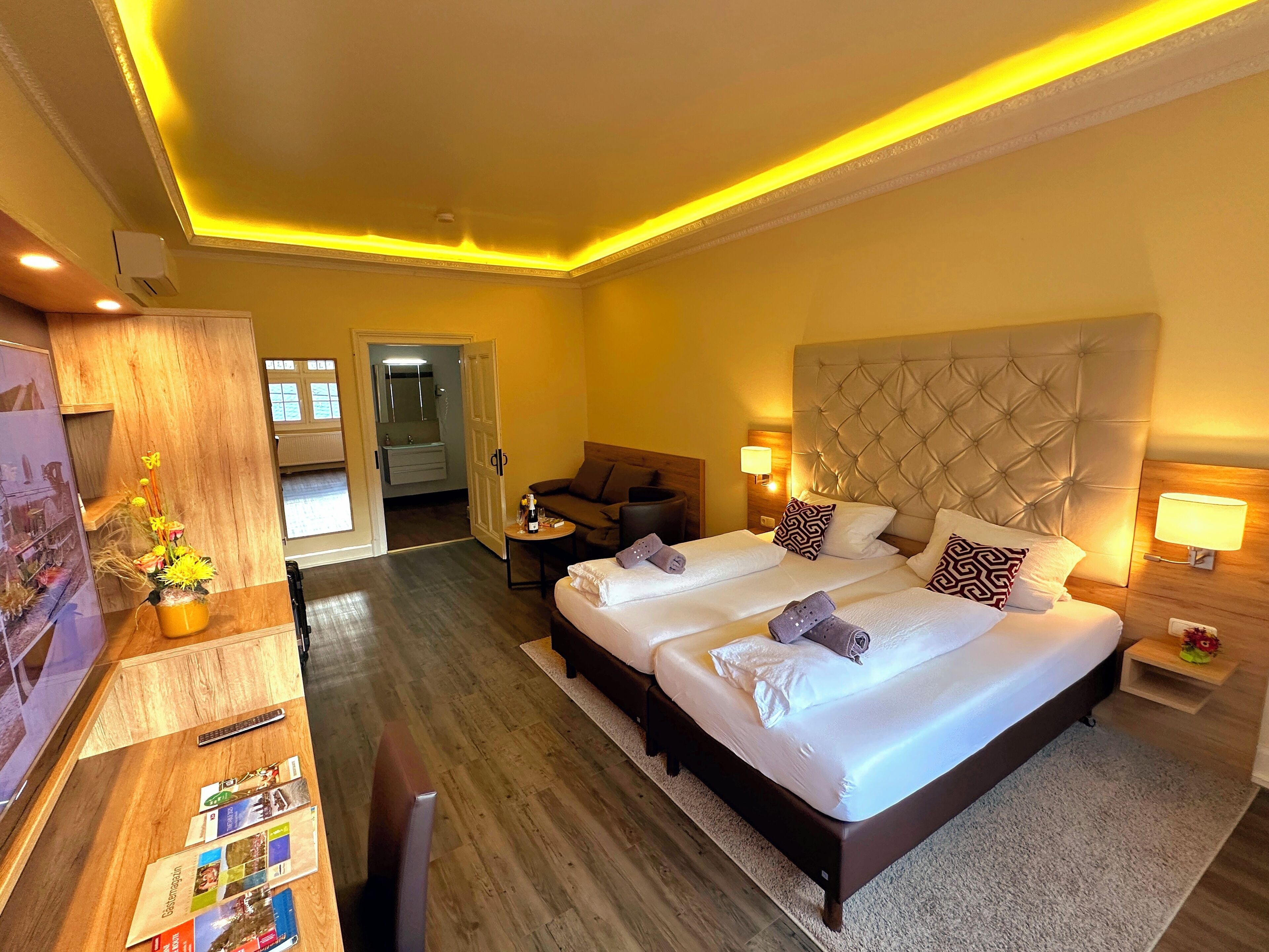A hotel room with a large bed, a desk, a chair, and a small table with a bottle and glasses.