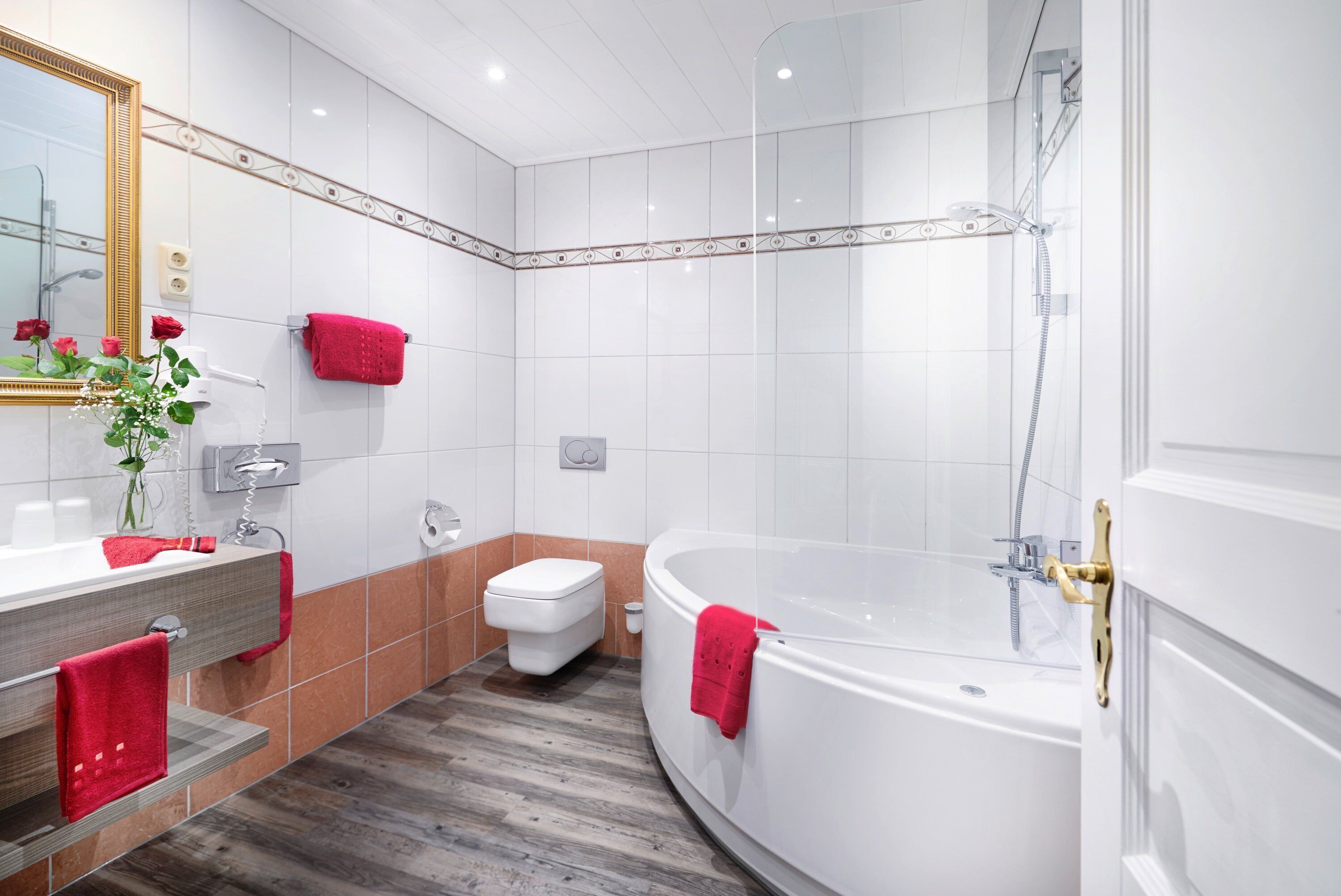 Ein modernes Badezimmer mit einer großen Badewanne, einer Toilette und einem Waschtisch inklusive Spiegel und Handtuchhalter.