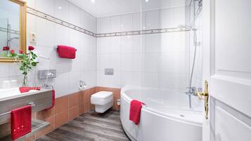 Ein modernes Badezimmer mit einer großen Badewanne, einer Toilette und einem Waschtisch inklusive Spiegel und Handtuchhalter.