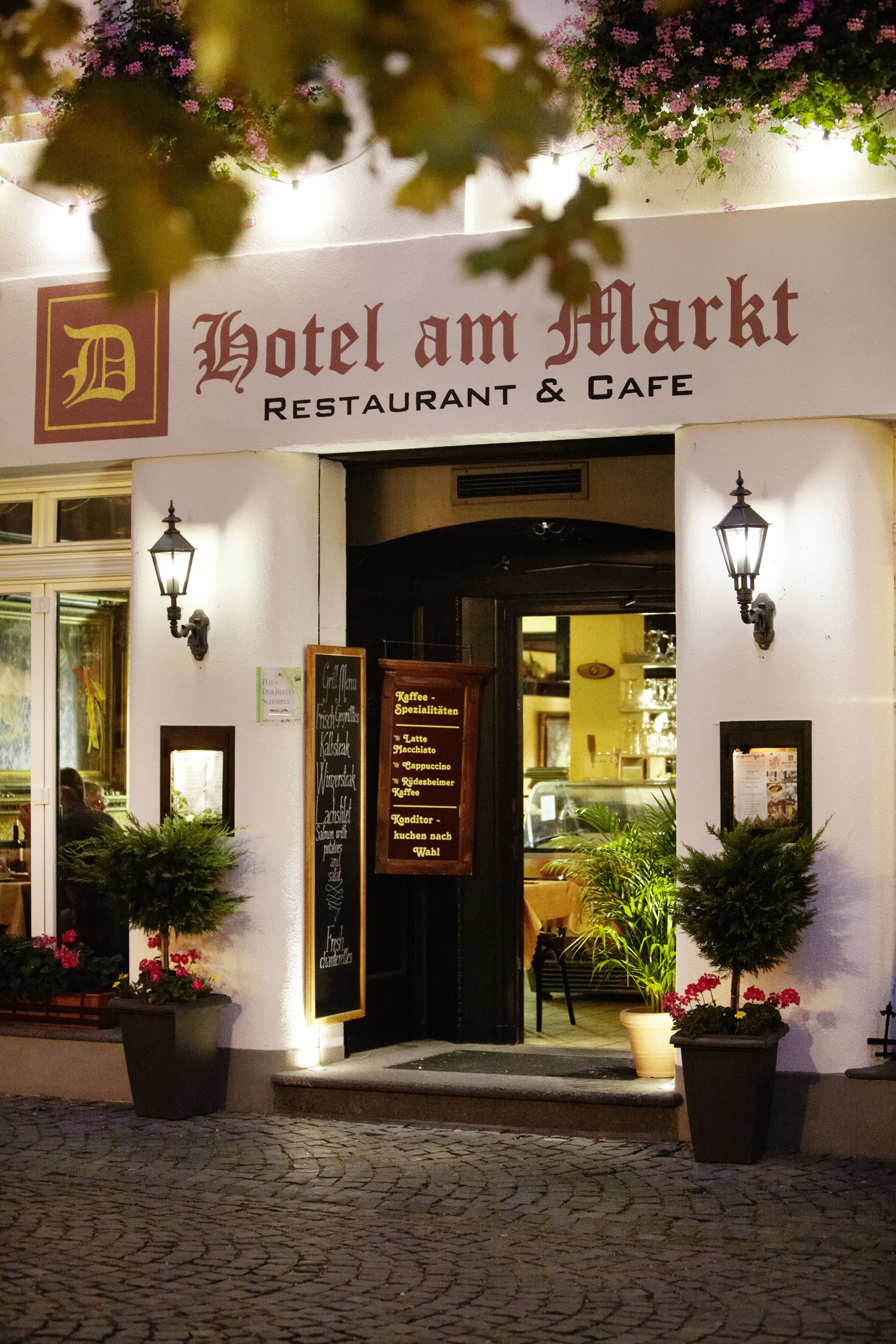 Der Eingang des Hotels am Markt mit einem Schild, das Kaffeespezialitäten auflistet, und einem Einblick in das Innere durch den Durchgang.