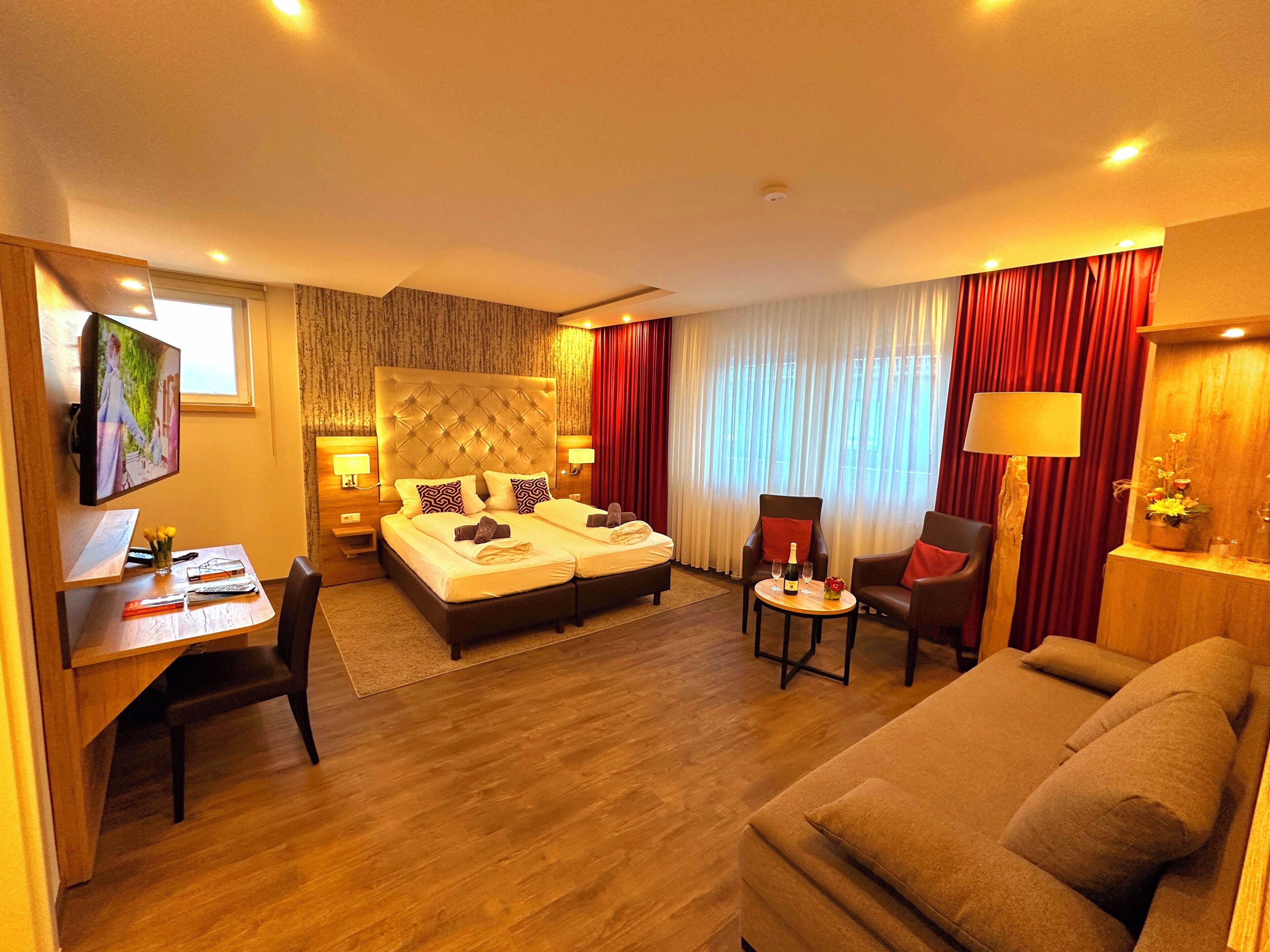 Ein Hotelzimmer mit Bett, Schreibtisch, Stuhl, Sofa und Fernseher.