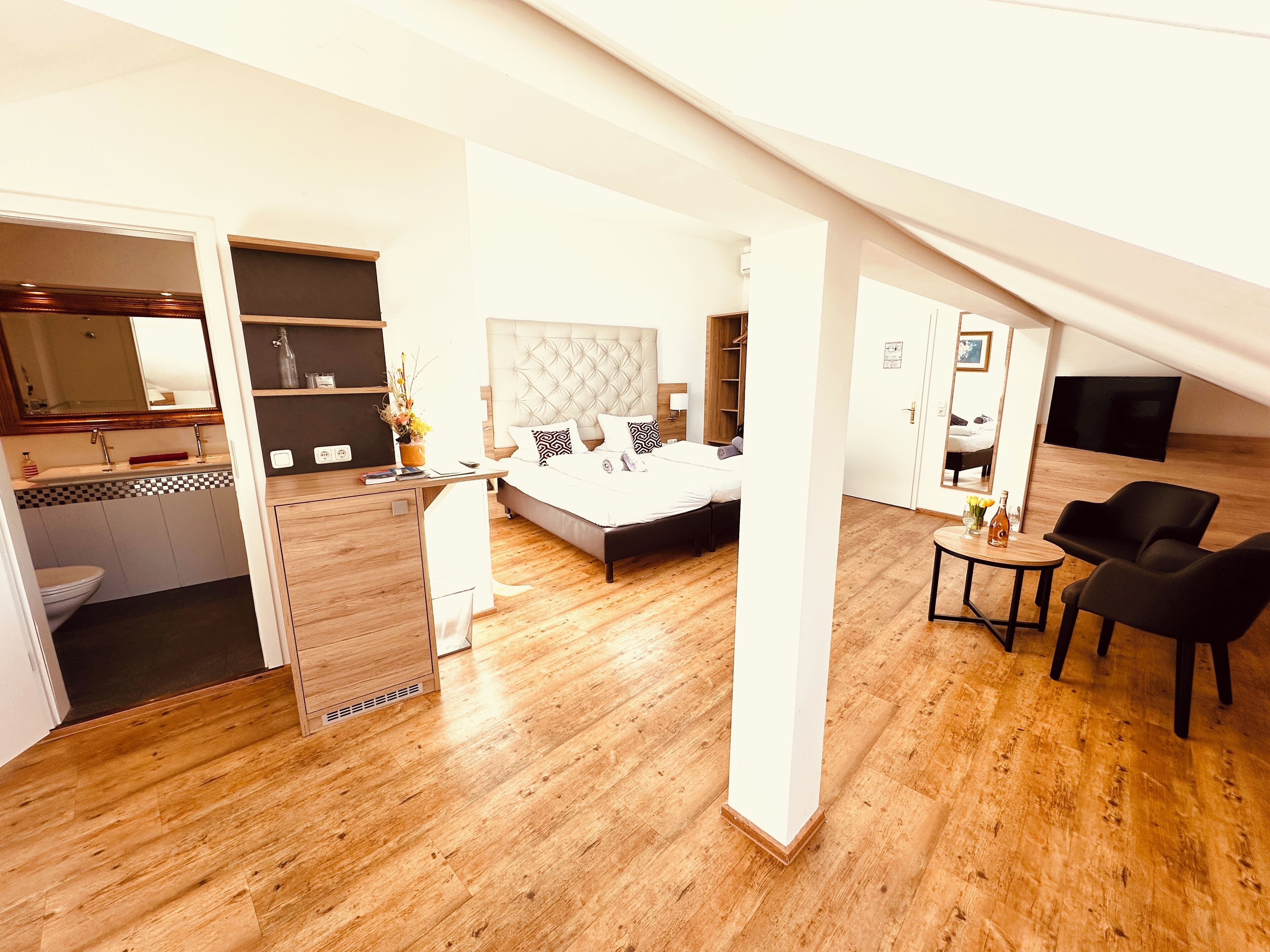 A modern bedroom with a large bed, a desk, and a TV.