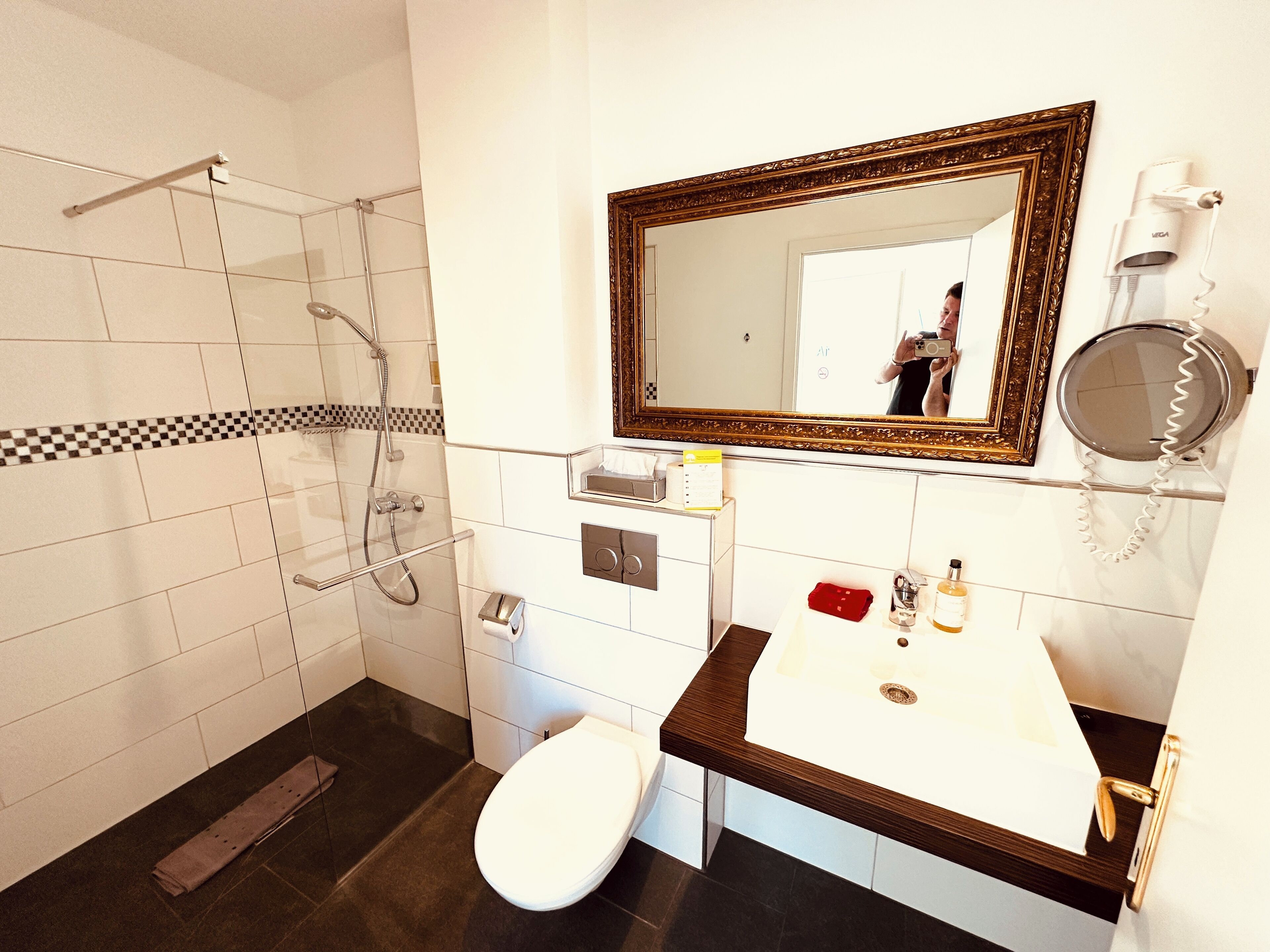 A bathroom with a shower, toilet, sink, and a mirror with a decorative frame.