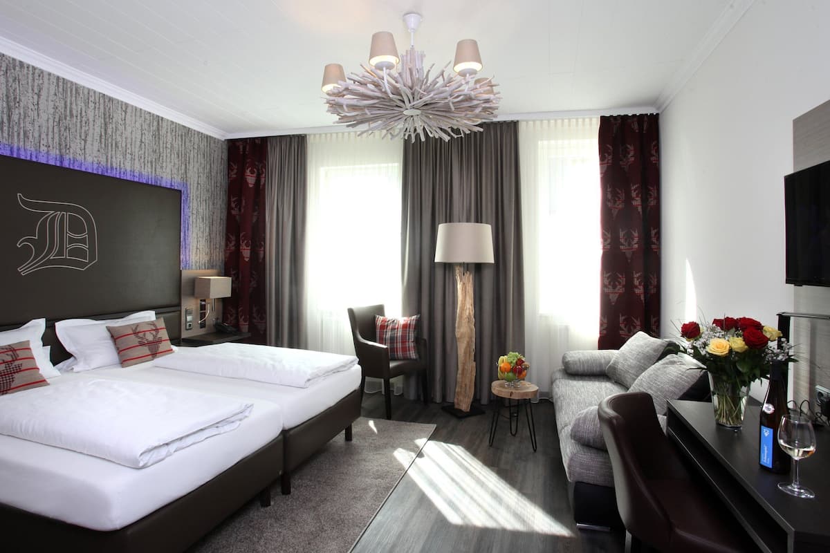 Ein modernes Hotelzimmer mit einem großen Bett, einer Couch, einem Schreibtisch mit Blumenvase und einem Fernseher.