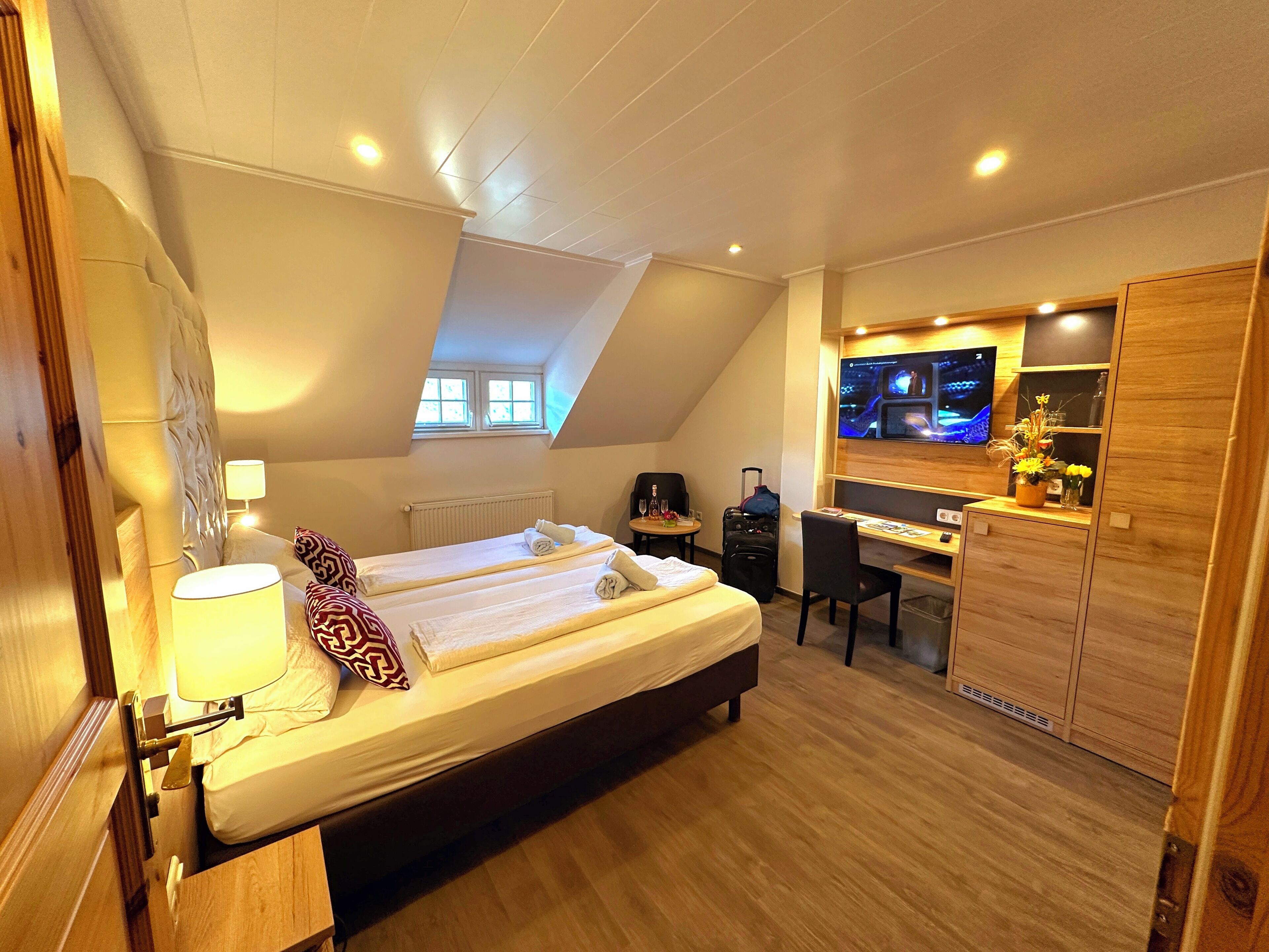 Habitación de hotel con cama, escritorio, silla, televisión y ventana pequeña.
