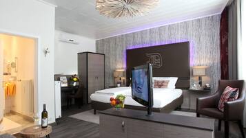 A modern hotel room with a large bed, a desk, a TV, and a dining area.
