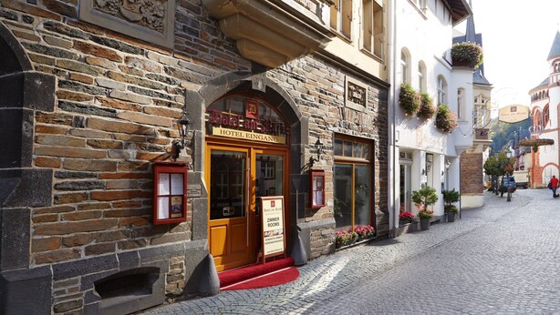 A historic stone building with a wooden entrance, a sign for 'Hotel Eingang', and a red carpet leading to the door. - HOTEL AM MARKT (Bacharach)