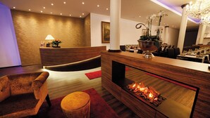 A modern lobby with a reception desk, a comfortable seating area, a fireplace, and a chandelier. - HOTEL AM MARKT (Bacharach)