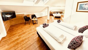 A modern loft bedroom with a large bed, a TV, a small table, and two chairs. - HOTEL AM MARKT (Bacharach)