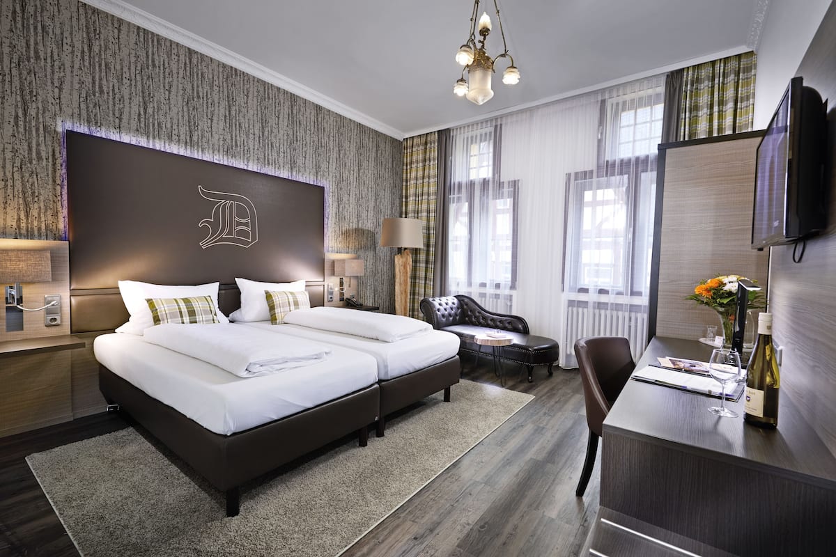 Ein Hotelzimmer mit einem großen Bett, einem Schreibtisch, einem Stuhl, einem Fernseher und einer Kristallleuchter.