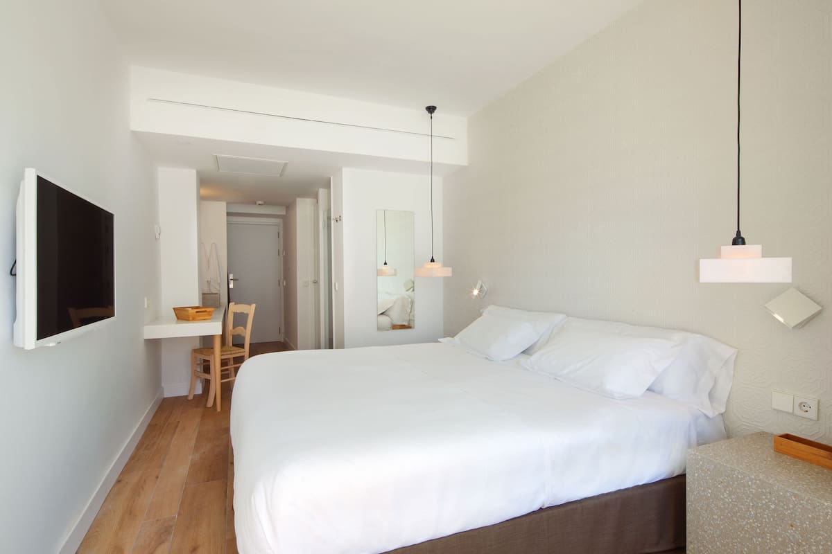 Un dormitorio con cama, escritorio, silla, televisor y lámpara de pared.