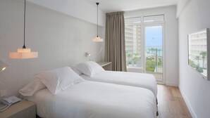 Habitación de hotel con dos camas, un teléfono en la mesita de noche, una ventana con vistas al mar y un papel tapiz estampado.