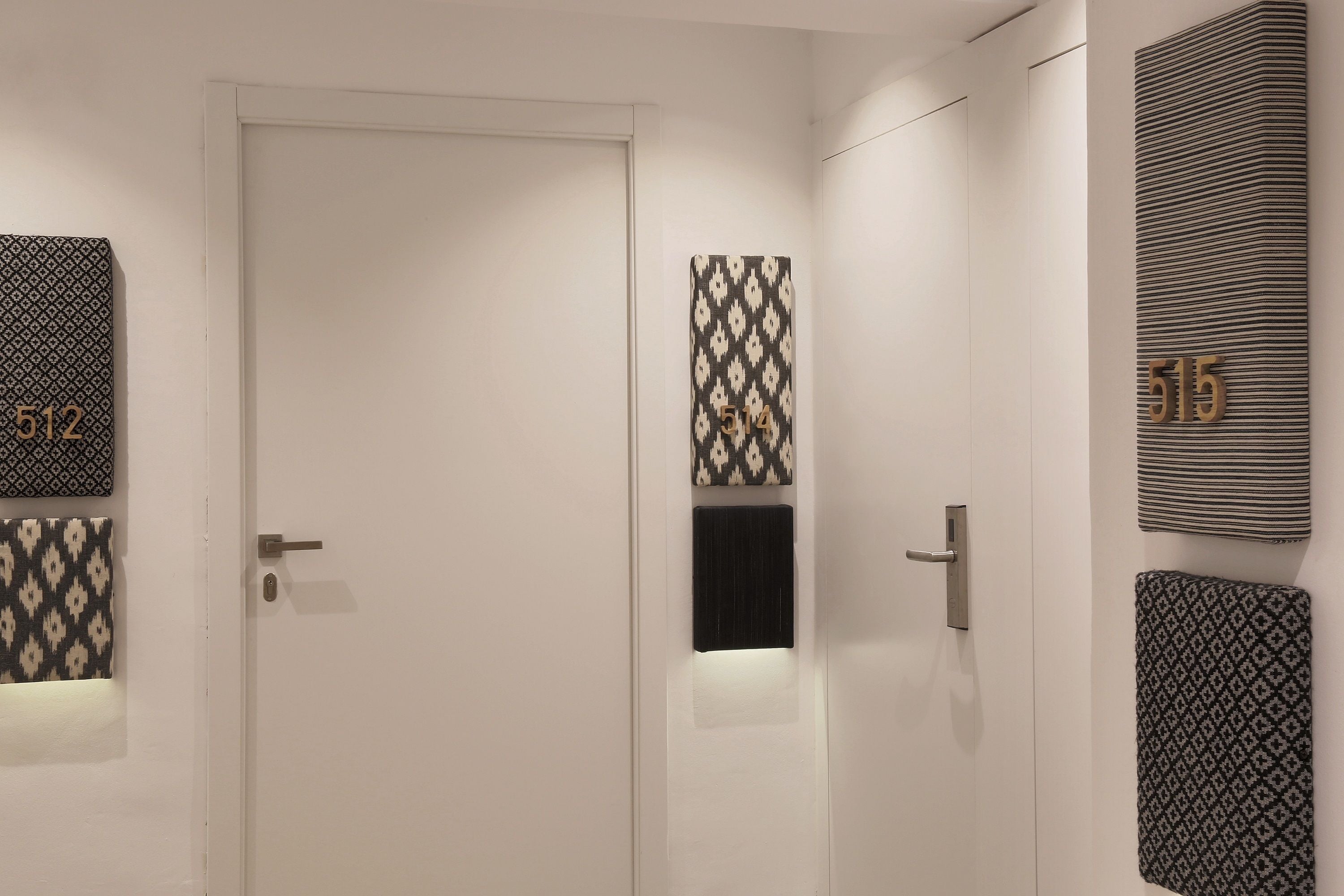 Un pasillo con una puerta blanca, decoración de pared con diseño y un letrero con el número 515.