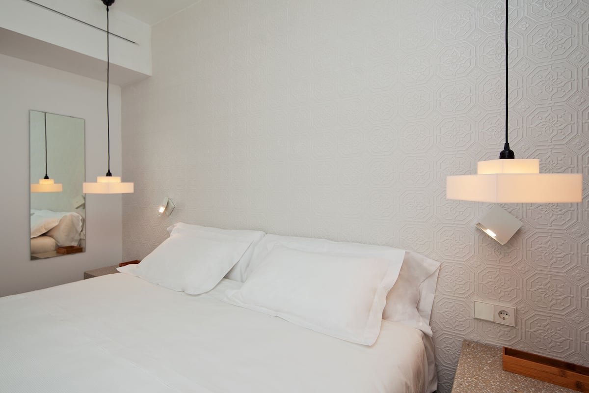 Una habitación de hotel moderna con una cama bien hecha, un espejo grande y lámparas colgantes.