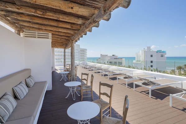 A rooftop terrace with a wooden pergola, white lounge chairs, and tables, overlooking a beach and buildings. - HM Balanguera Beach- Adults Only (Palma de Mallorca)