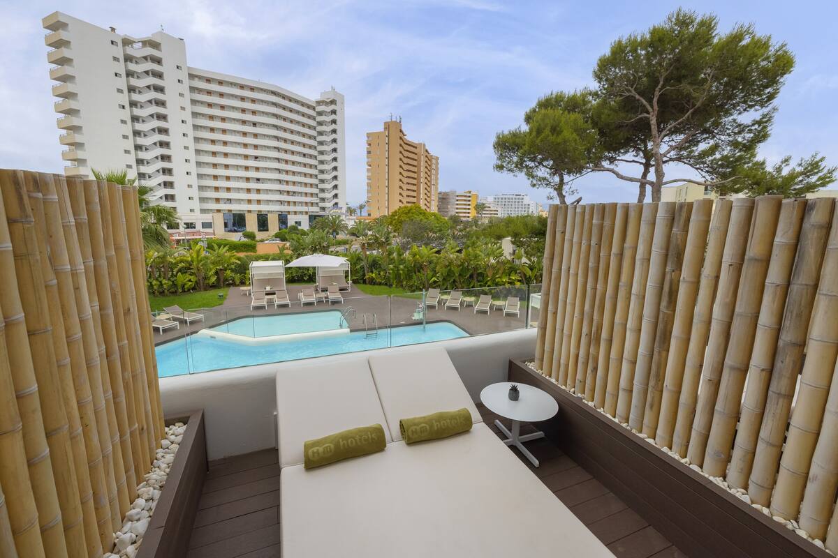 Un área de piscina en la azotea con sillones, una mesita y vistas de edificios circundantes.