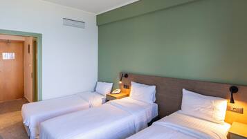Ein Hotelzimmer mit zwei Einzelbetten, einem hölzernen Kopfteil, einem Nachttisch mit Lampe und einer Wand in Grüntönen.