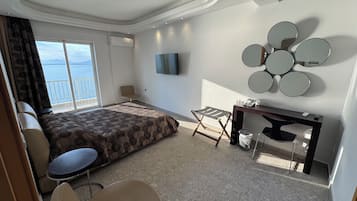 A hotel room with a bed, a desk, a chair, a TV, and a view of the sea.