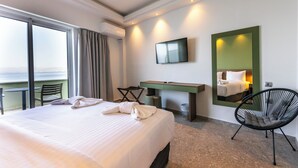 A hotel room with a large bed, a desk, a chair, a TV, and a view of the sea. - Messinian Bay Hotel (Kalamata)