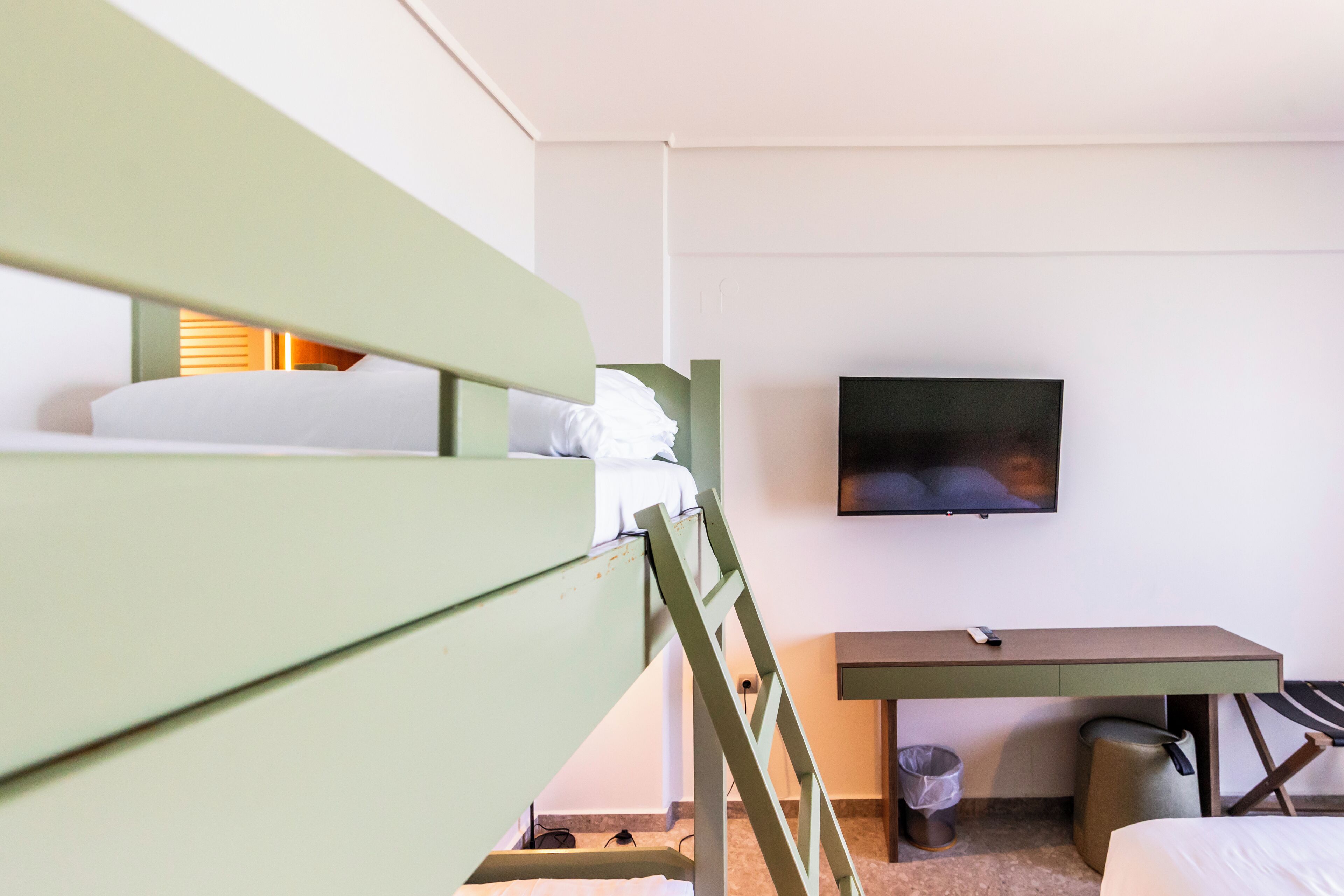 A hotel room with a bunk bed, a desk, a television, and a trash bin.