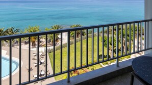 A balcony with a view of the sea, a pool, and a grassy area with chairs and tables. - Messinian Bay Hotel (Kalamata)