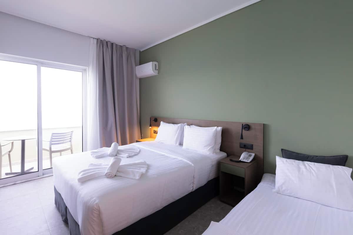 Habitación de hotel con una cama grande, una mesita de noche con teléfono, una ventana con cortinas y vistas al exterior.