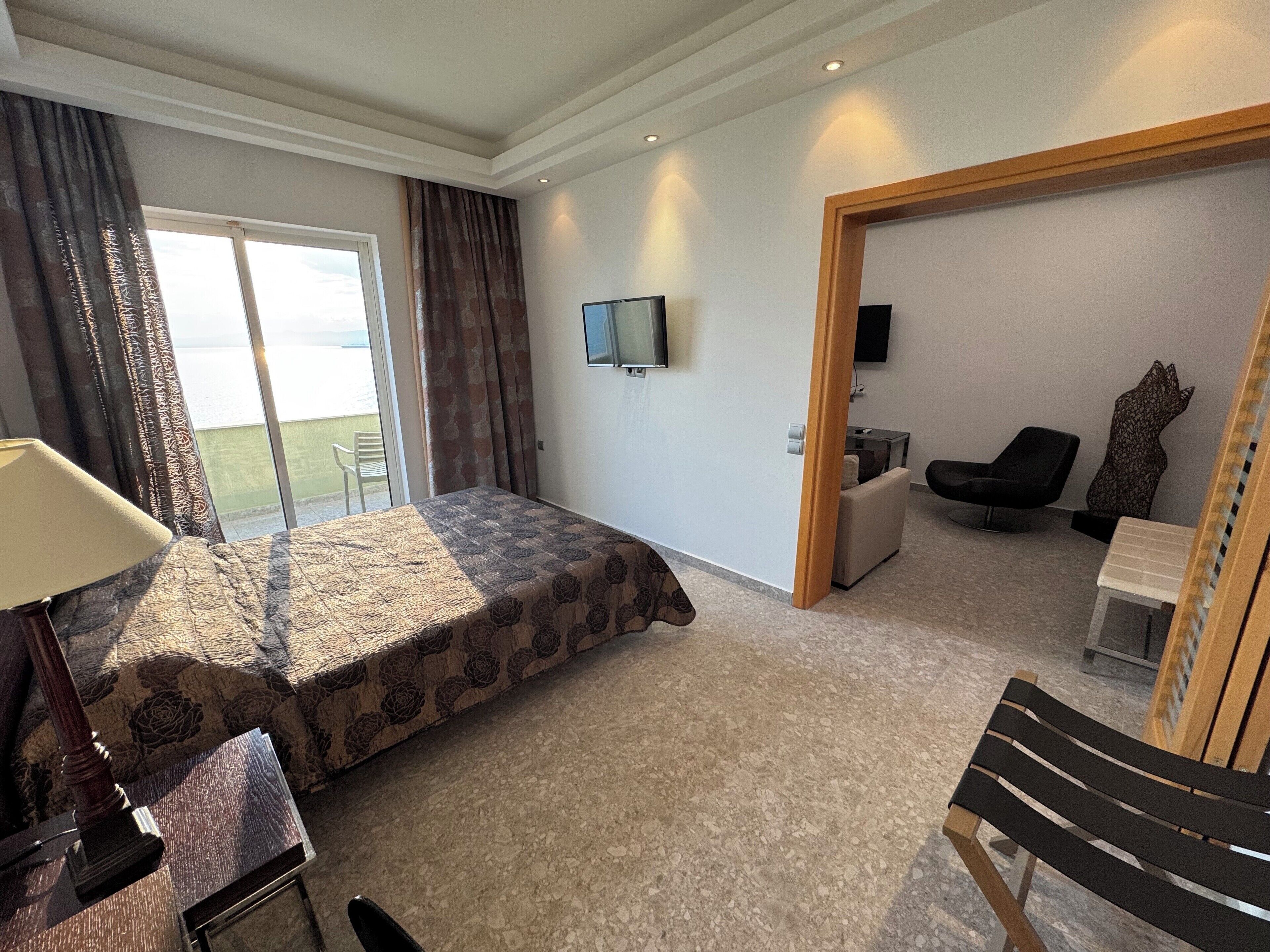 Una habitación de hotel con cama, escritorio, silla, televisión y balcón.