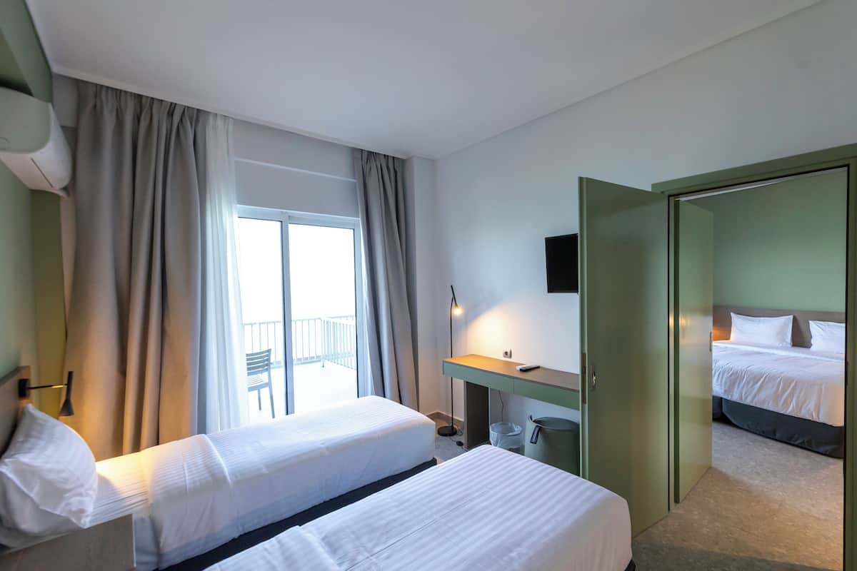 Habitación de hotel con dos camas, un escritorio, una silla, un balcón y un televisor.
