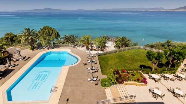 A pool with a view of the sea, outdoor seating, and palm trees. - Messinian Bay Hotel (Kalamata)