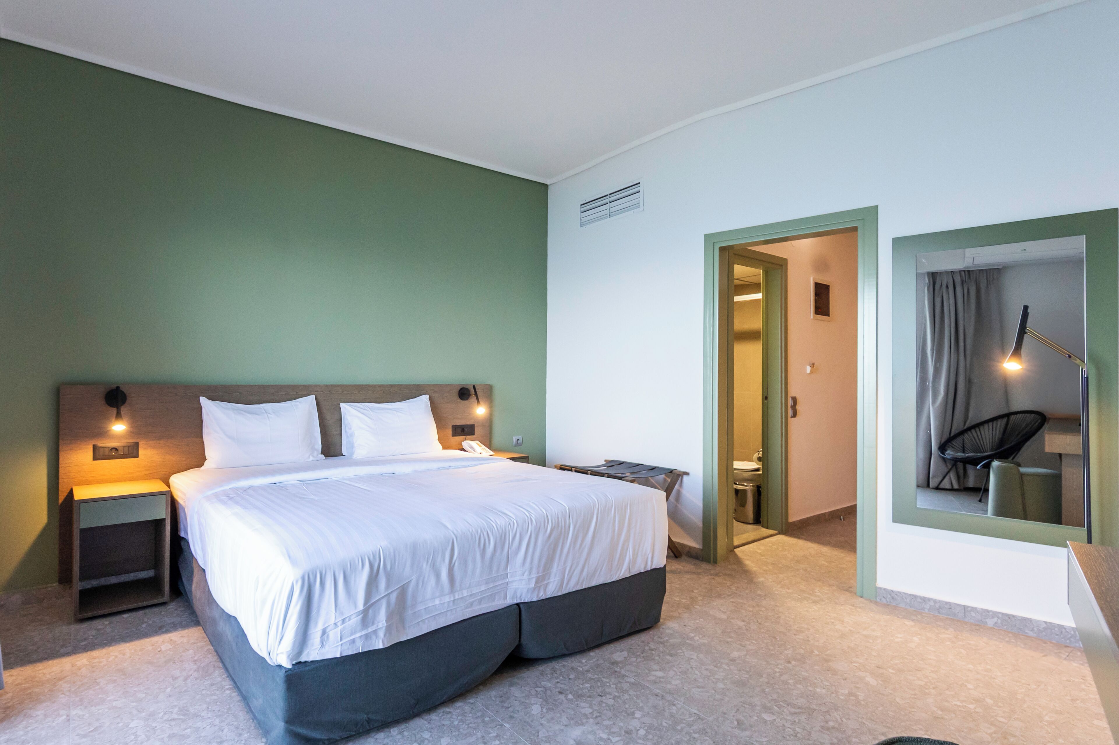 A modern hotel room with a large bed, bedside lamps, a small table, and a mirror.