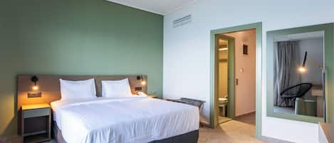 A modern hotel room with a large bed, bedside lamps, a small table, and a mirror.