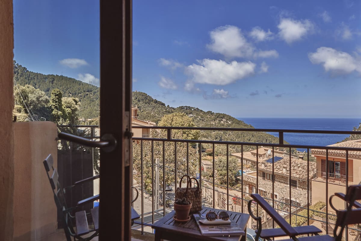 A balcony with a table, chairs, and a view of the sea and hills.