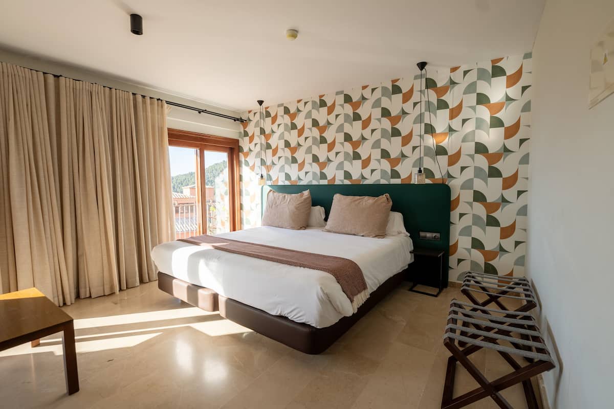 A modern hotel room with a large bed, a small table, and a view of the outdoors.