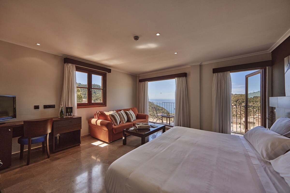 Une chambre avec un grand lit, un bureau, un canapé et un balcon avec vue.