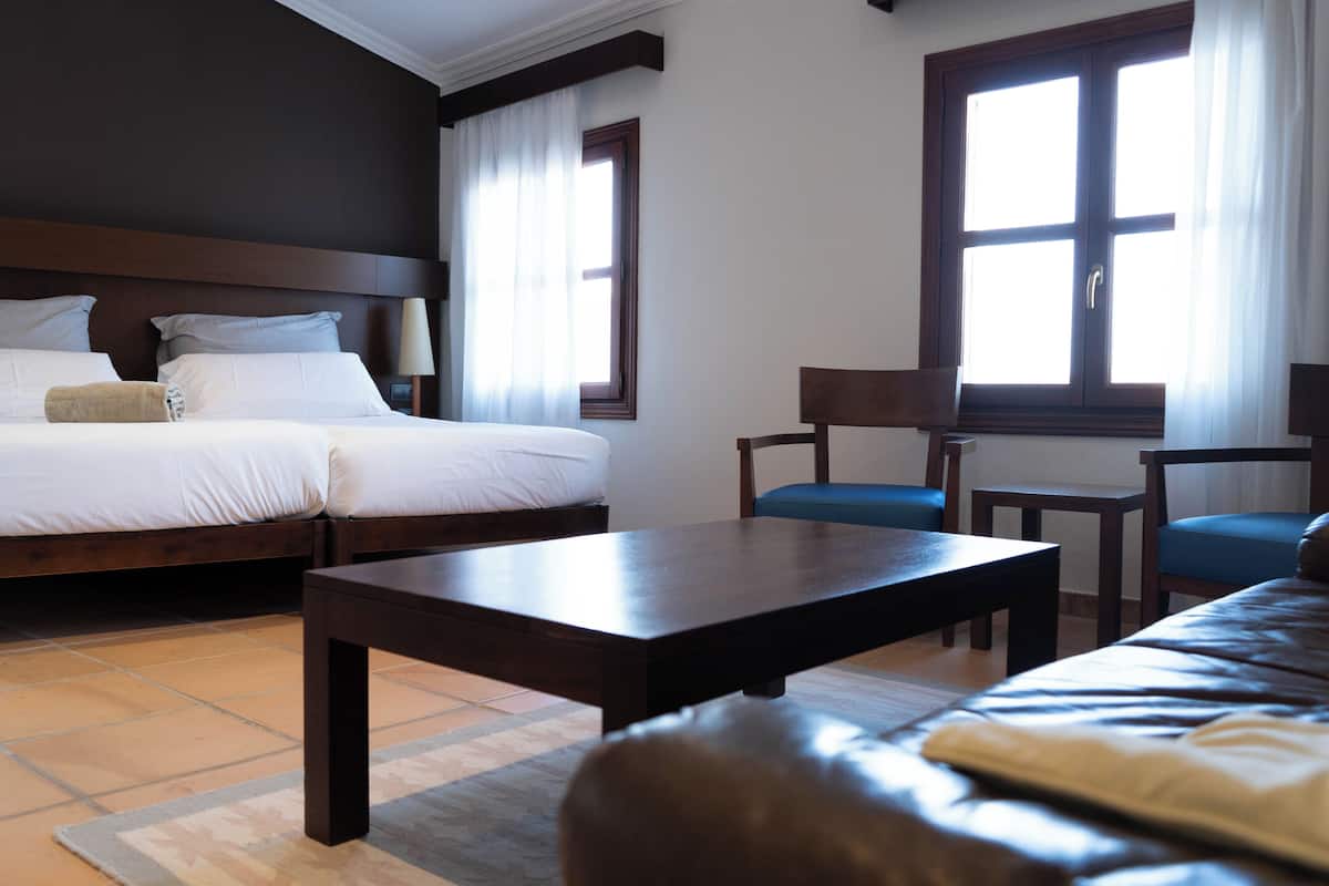 A hotel room with a bed, a sofa, a small table, and a window with curtains.