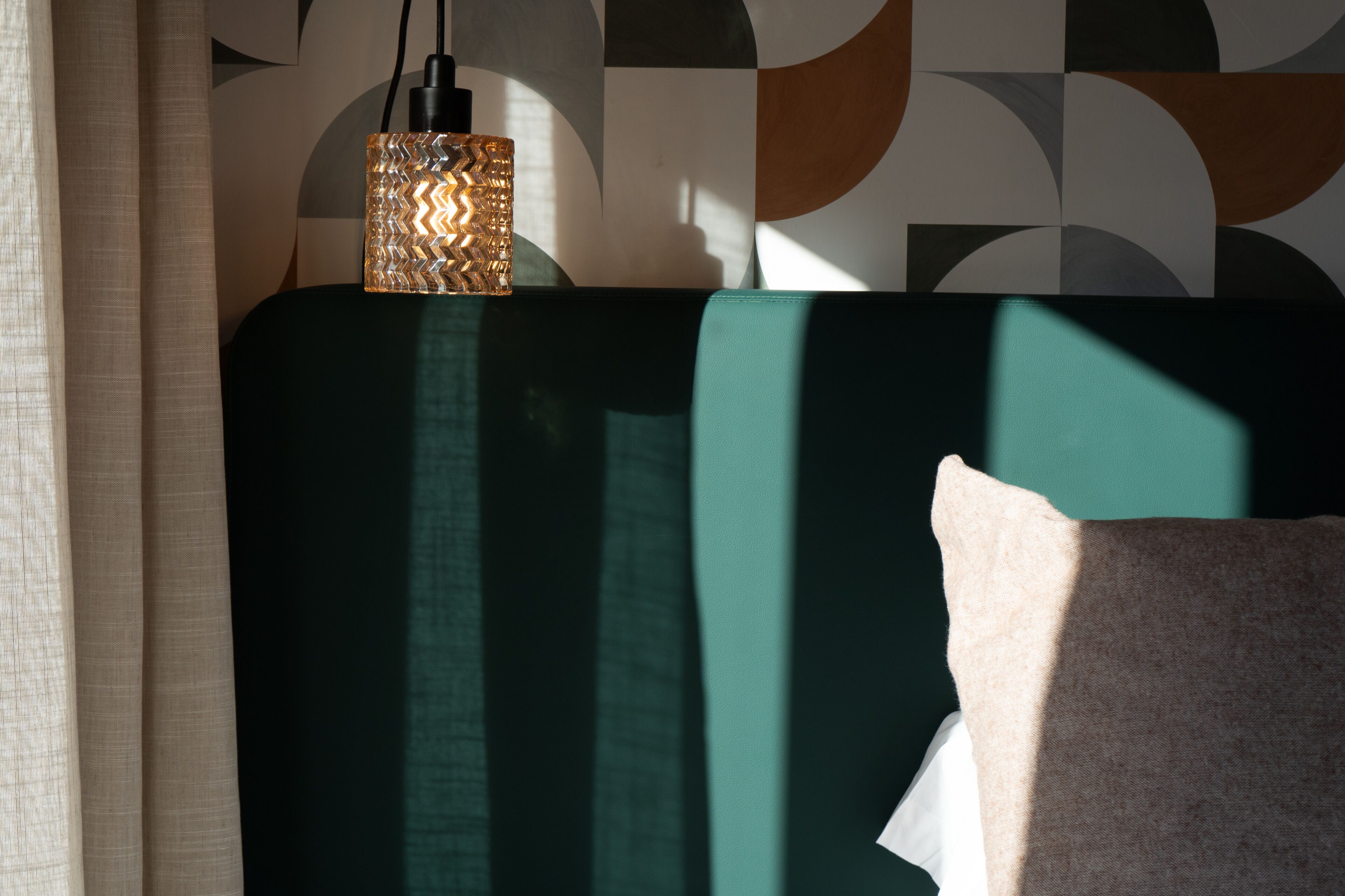 A room with a green headboard, a patterned lamp, and a pillow.