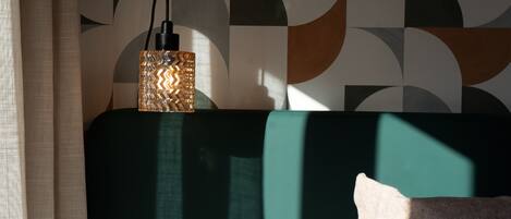 A room with a green headboard, a patterned lamp, and a pillow.