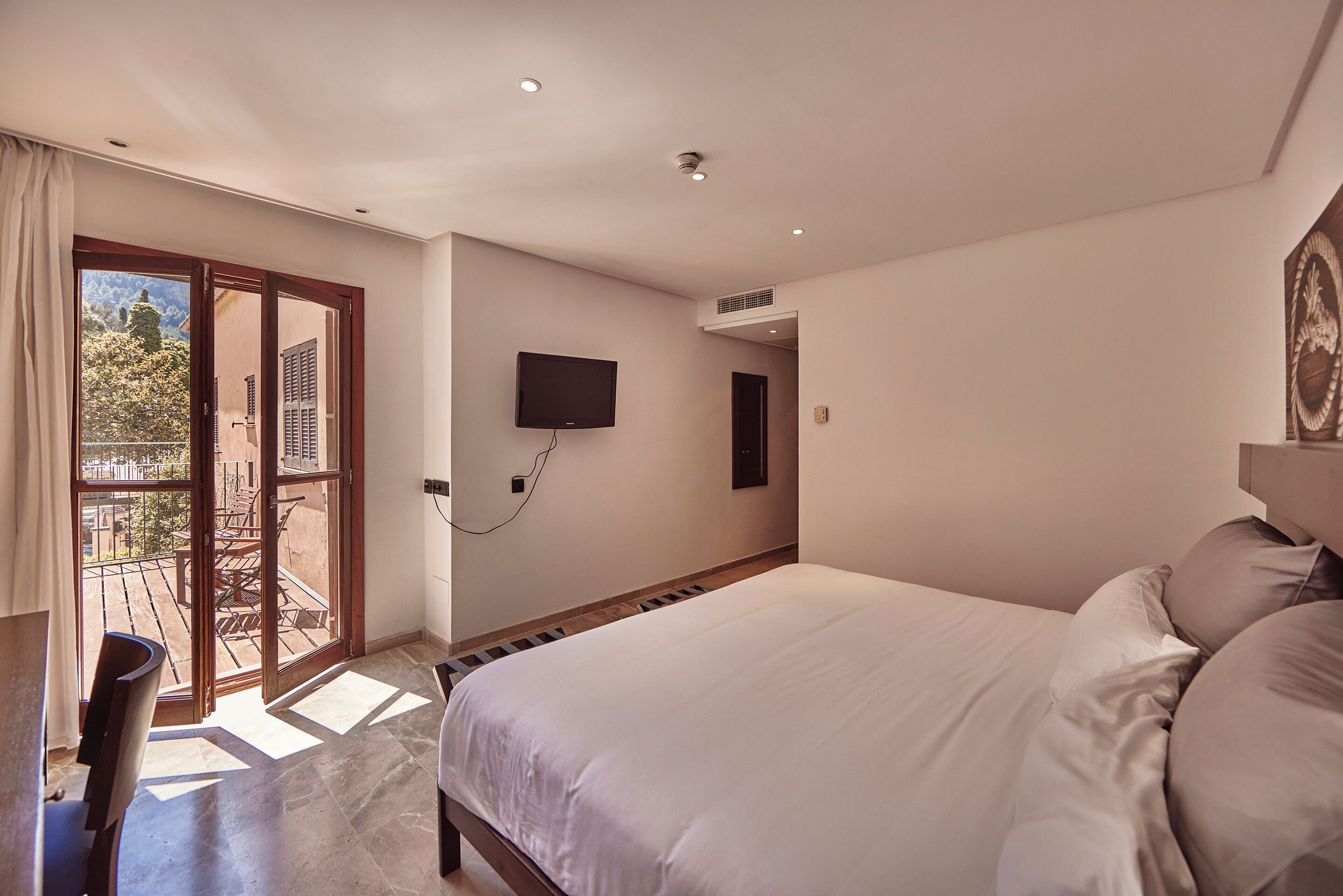 A bedroom with a large bed, a TV mounted on the wall, and a sliding glass door leading to an outdoor area.