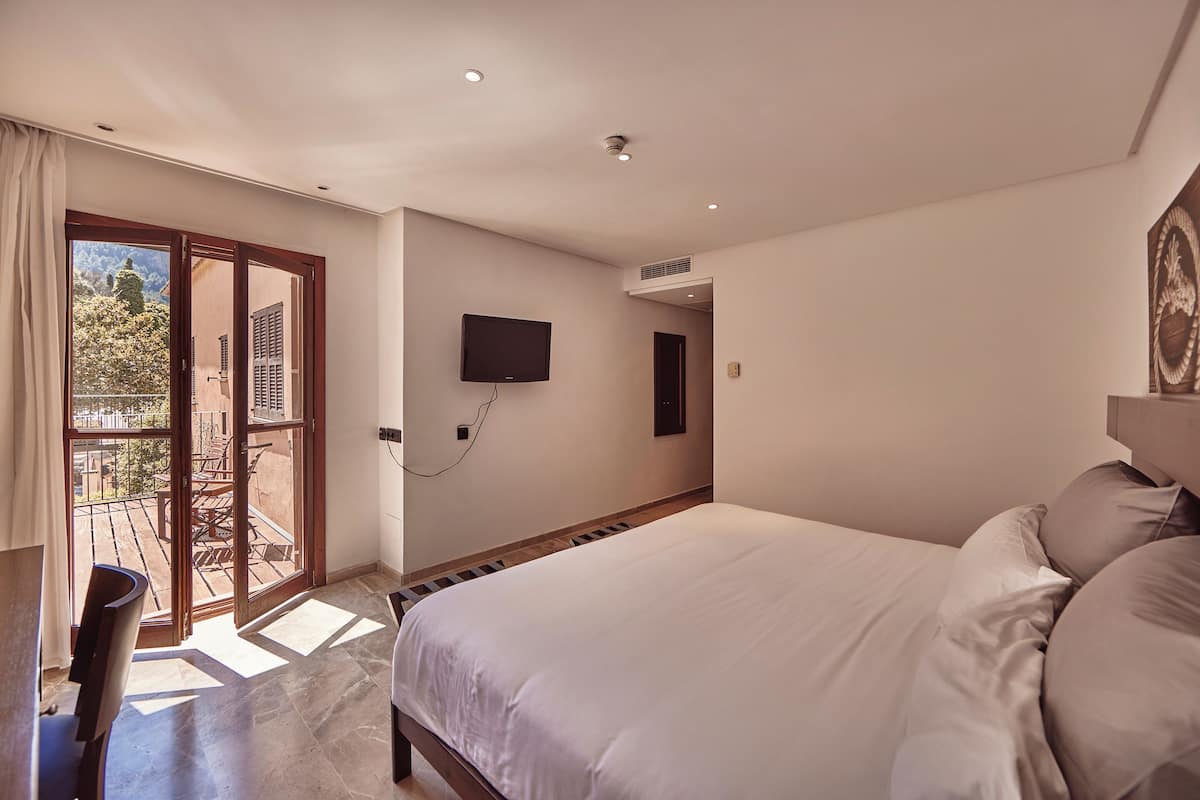 A bedroom with a large bed, a TV mounted on the wall, and a sliding glass door leading to an outdoor area.