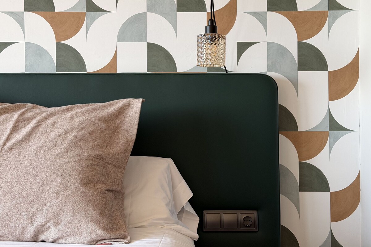 Un lit avec une tête de lit, un mur orné d’un motif géométrique et une suspension lumineuse.