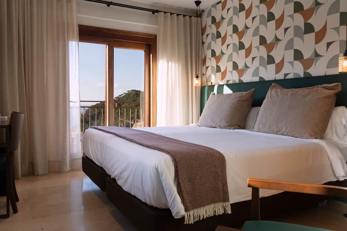 A bedroom with a bed, a desk, a chair, a balcony, and a patterned wall.