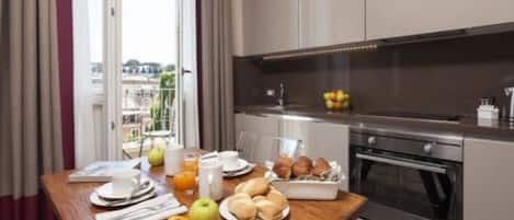 A breakfast setup with a table, breakfast items, and a kitchen area with appliances.