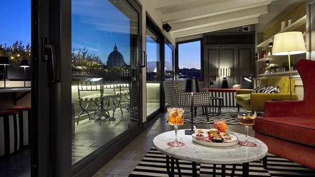 A modern dining area with a glass wall, a round table with drinks, and a red sofa.