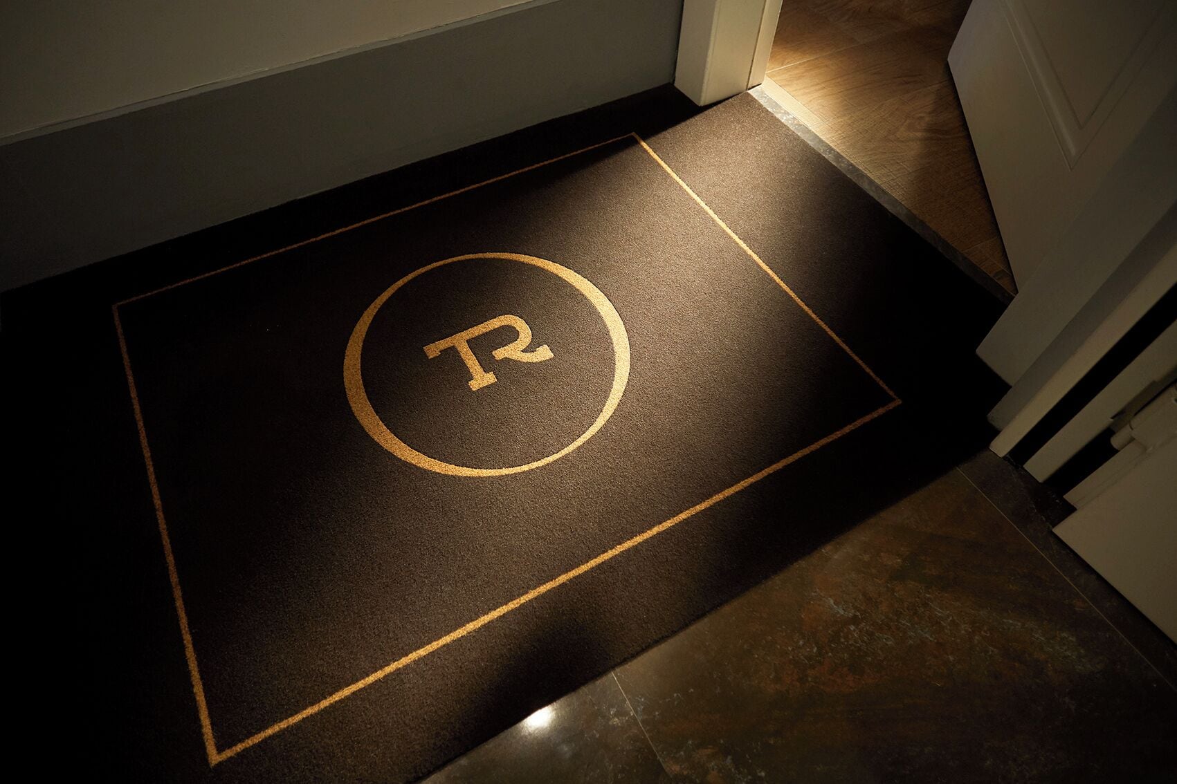 A doormat with a large 'R' and a circle, indicating a specific room or area.